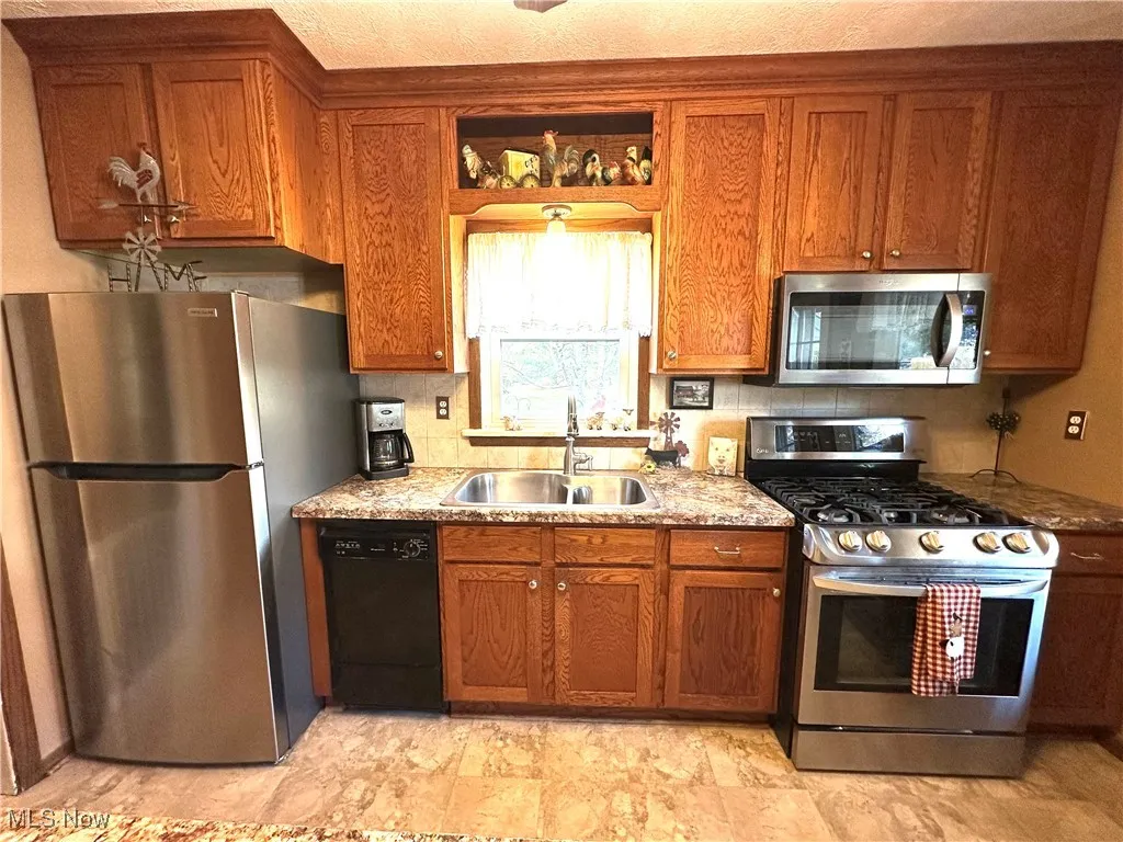 Kitchen with appliances with stainless steel finishes, brown cabinets, and light stone counters