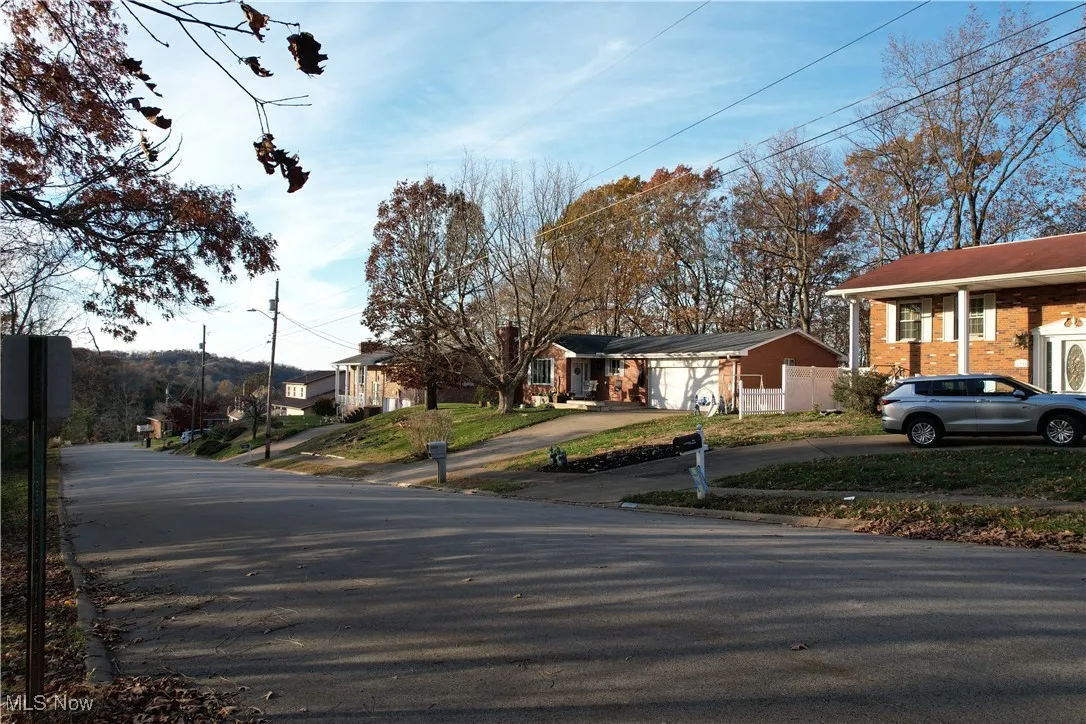 View of asphalt street featuring curbs, a residential view, street lighting, and traffic signs