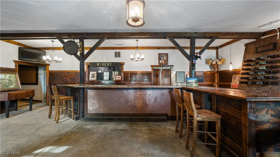 Bar area with wainscoting, hanging light fixtures, a textured ceiling, wooden walls, and a chandelier