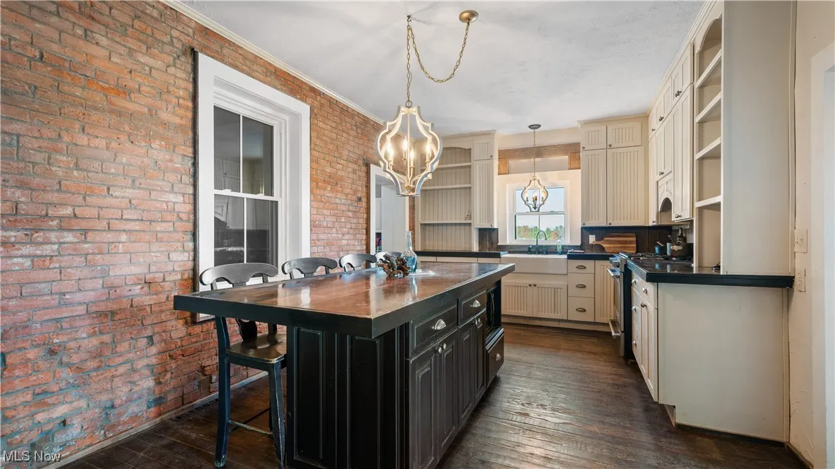 Kitchen featuring dark cabinets, cream cabinets, open shelves, decorative light fixtures, and dark wood-style floors