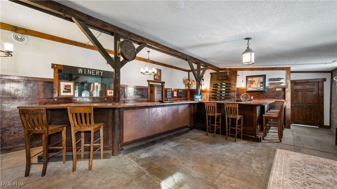Indoor dry bar featuring a chandelier, a textured ceiling, pendant lighting, beamed ceiling, and dark countertops