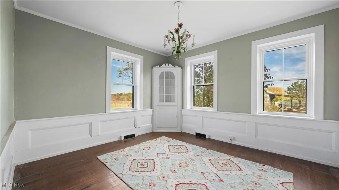 Unfurnished dining area featuring ornamental molding, a wainscoted wall, dark wood finished floors, a decorative wall, and a chandelier