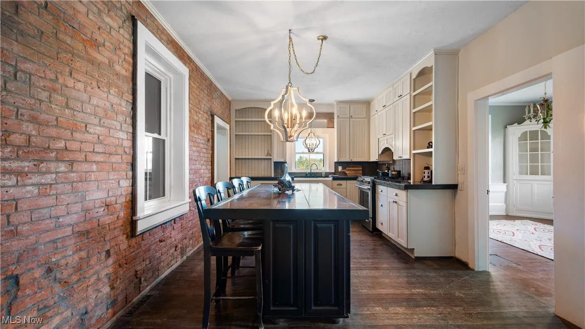 Kitchen with a chandelier, dark wood-style flooring, dark countertops, open shelves, and brick wall