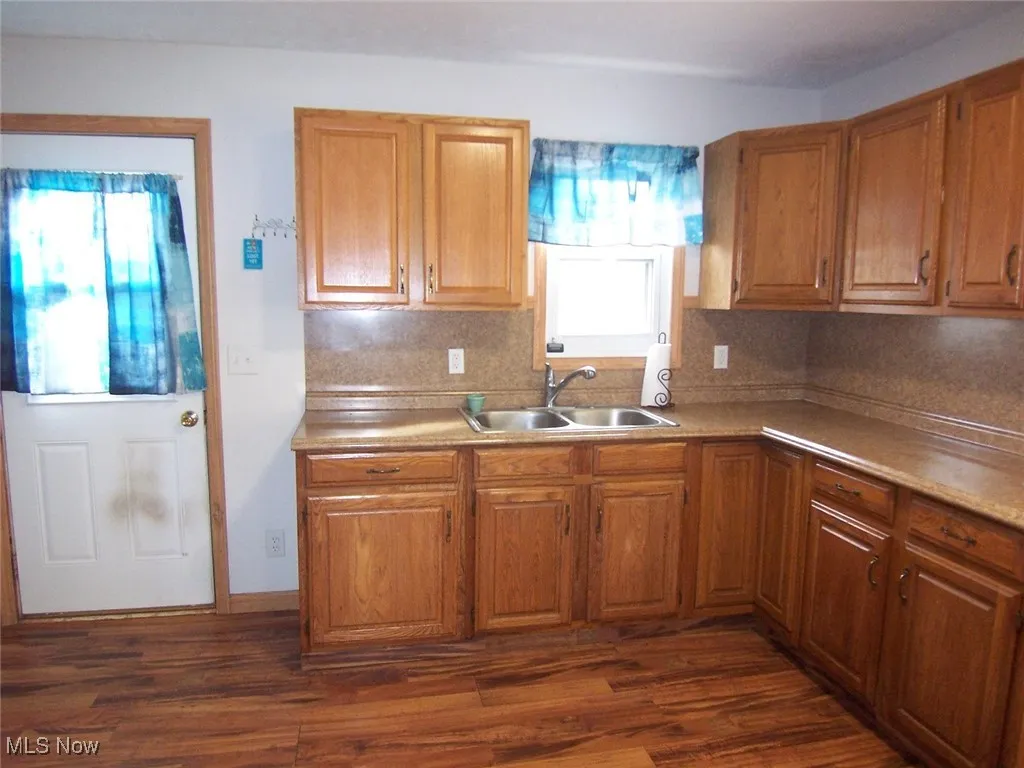 Kitchen featuring brown cabinetry, light countertops, dark wood-type laminate flooring, and backsplash