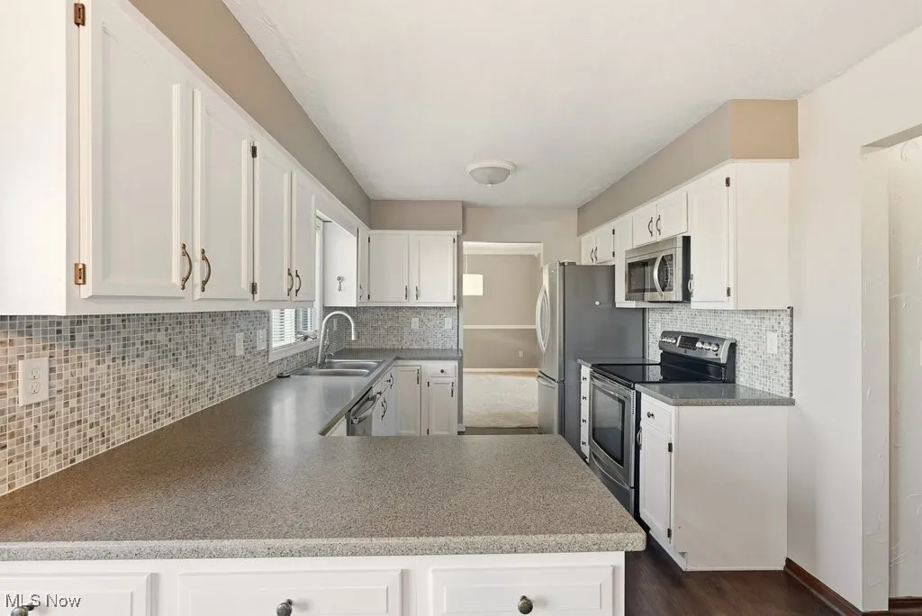 Kitchen with appliances with stainless steel finishes, tasteful backsplash, white cabinets, a peninsula, and dark wood-style floors