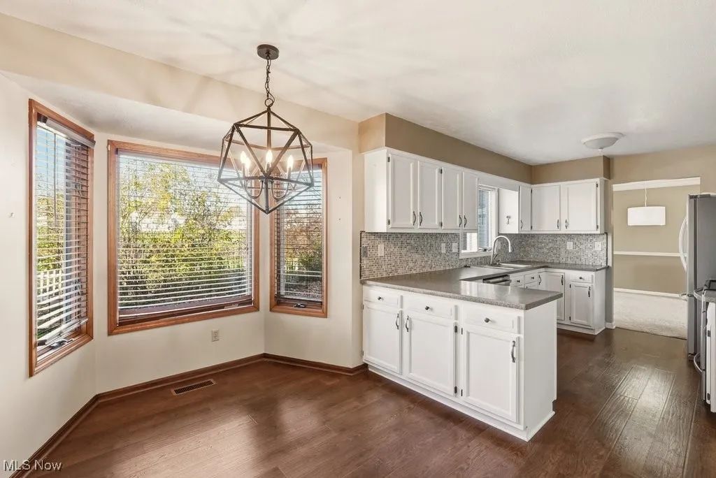 Kitchen with hanging light fixtures, white cabinets, a peninsula, and dark wood-type flooring
