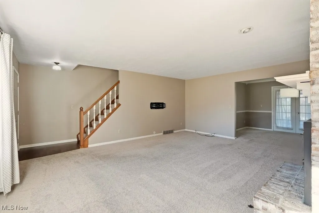 Unfurnished living room with carpet, stairs, and french doors