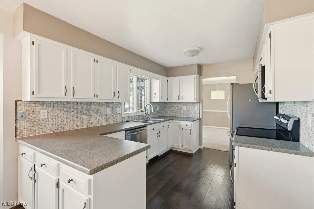 Kitchen with decorative backsplash, white cabinets, electric range oven, and a peninsula