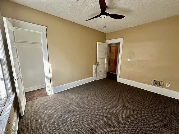 Unfurnished bedroom featuring dark carpet, a textured ceiling, and a ceiling fan