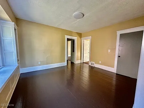 Empty room with a textured ceiling and dark wood-style flooring