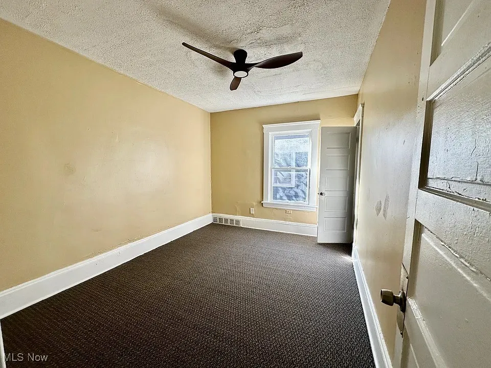 Empty room with dark carpet, a textured ceiling, and ceiling fan