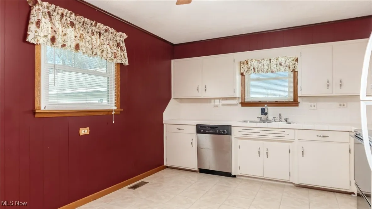 Kitchen featuring dishwasher, white cabinets, range, tile counters, and decorative backsplash