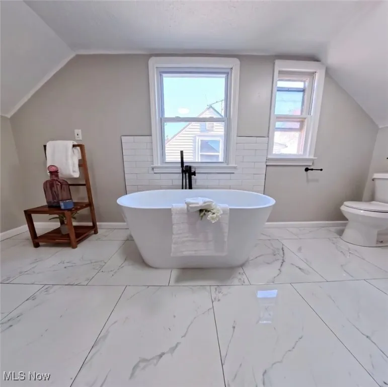 Bathroom featuring a freestanding tub, lofted ceiling, and light marble finish floors
