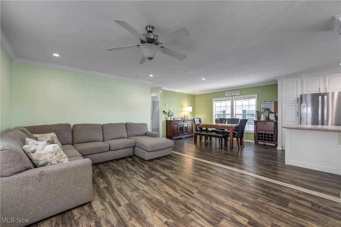 Living room with dark wood finished floors, ornamental molding, recessed lighting, and a ceiling fan