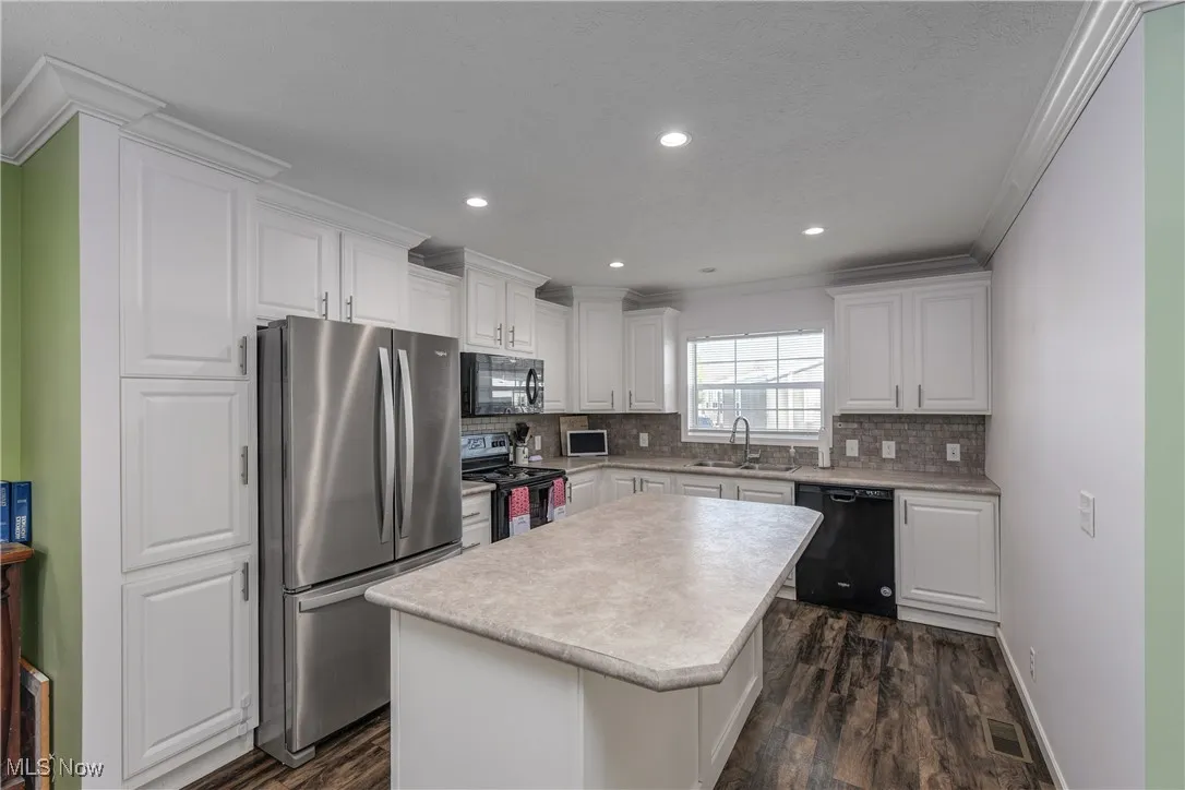 Kitchen featuring black appliances, crown molding, white cabinets, light countertops, and a center island
