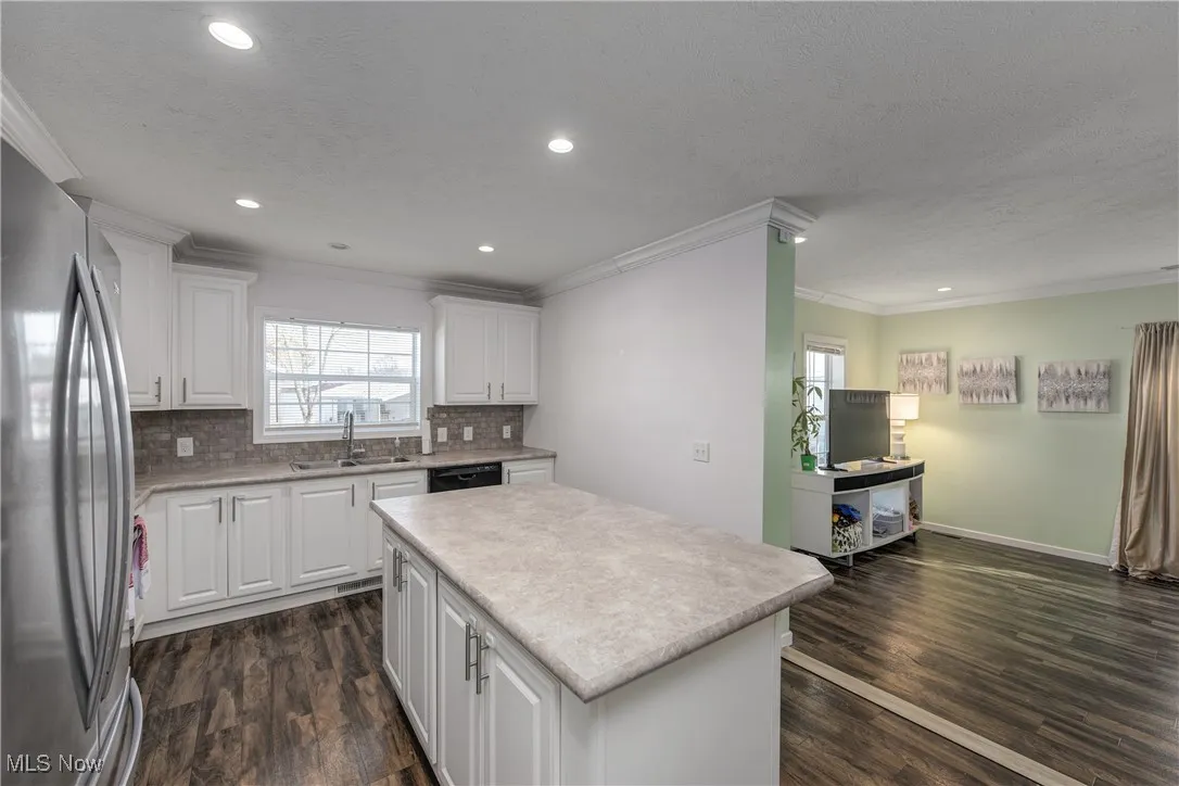 Kitchen featuring white cabinetry, ornamental molding, freestanding refrigerator, light countertops, and dark wood finished floors