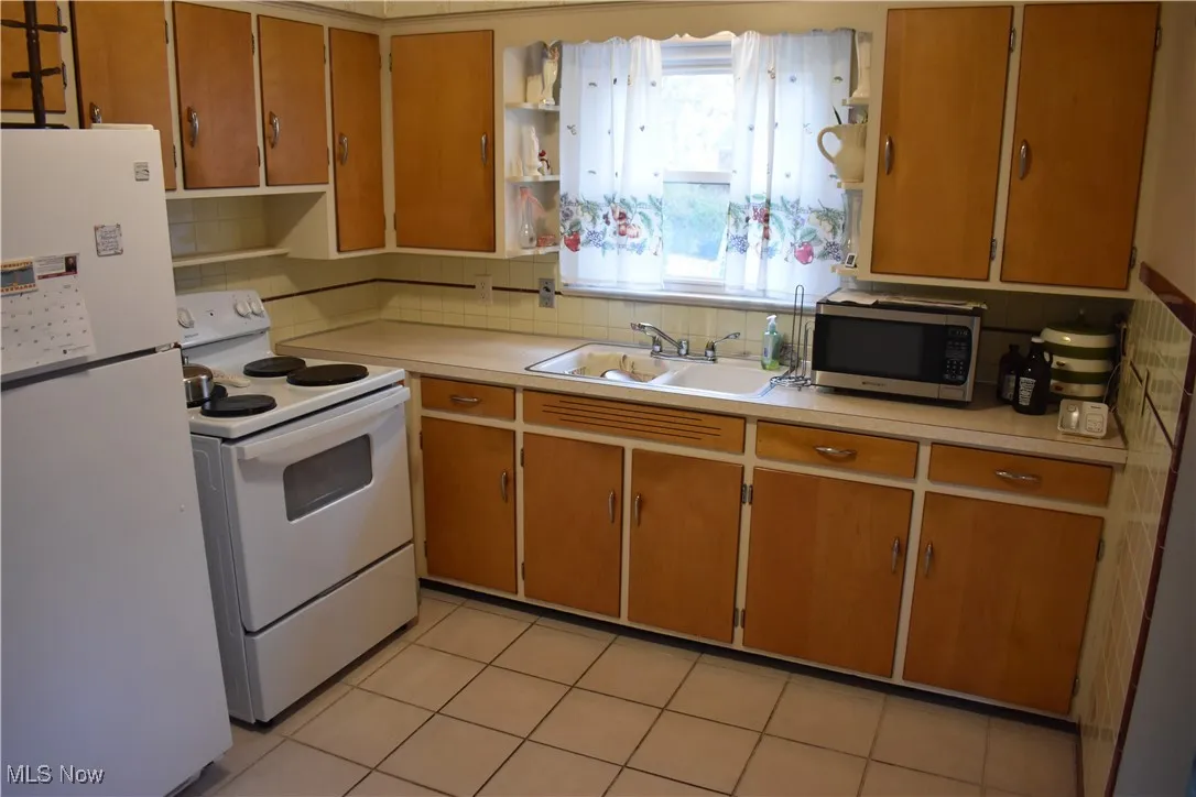 Kitchen featuring open shelves, white appliances, and light countertops