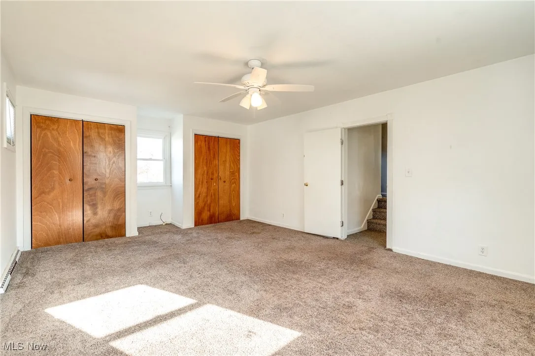 Unfurnished bedroom with multiple closets, carpet floors, ceiling fan, and baseboard heating