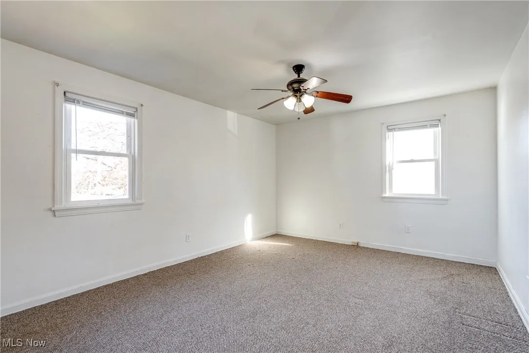 Carpeted empty room with baseboards and a ceiling fan