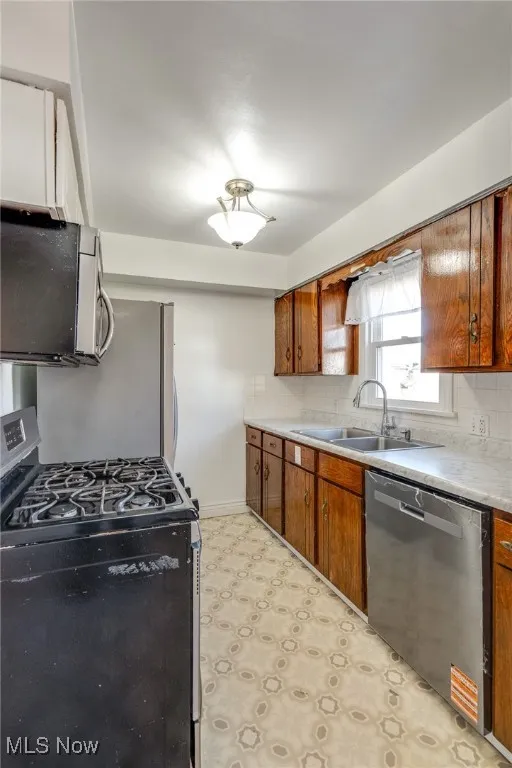 Kitchen featuring stainless steel appliances, brown cabinets, tasteful backsplash, and light countertops