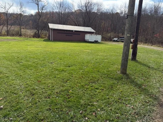 View of green lawn featuring an outbuilding, a wooded view, and a pole building