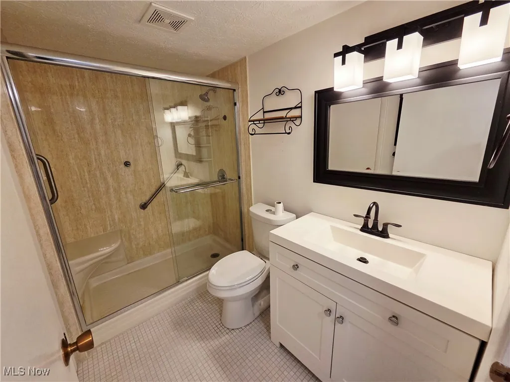 Full bathroom with a textured ceiling, vanity, a stall shower, and tile patterned floors