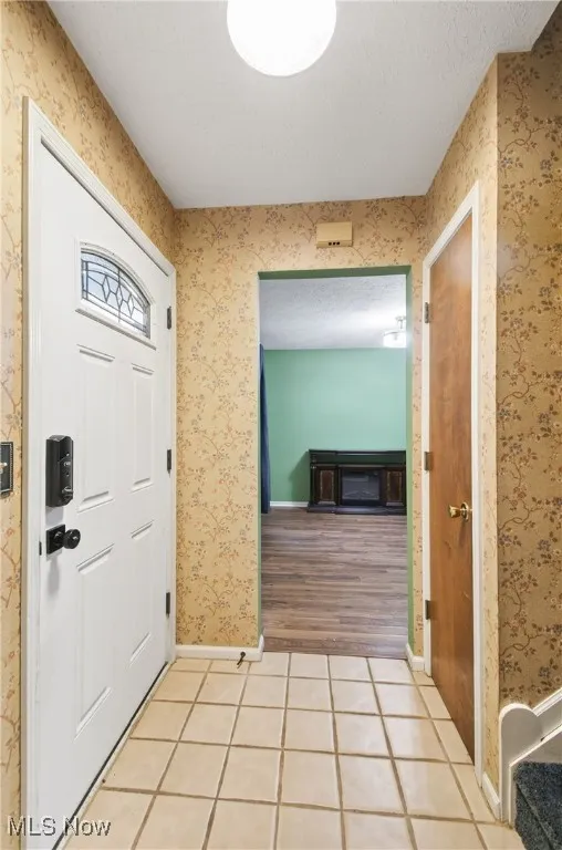 Entrance foyer with tile patterned flooring, wallpapered walls, and a textured ceiling
