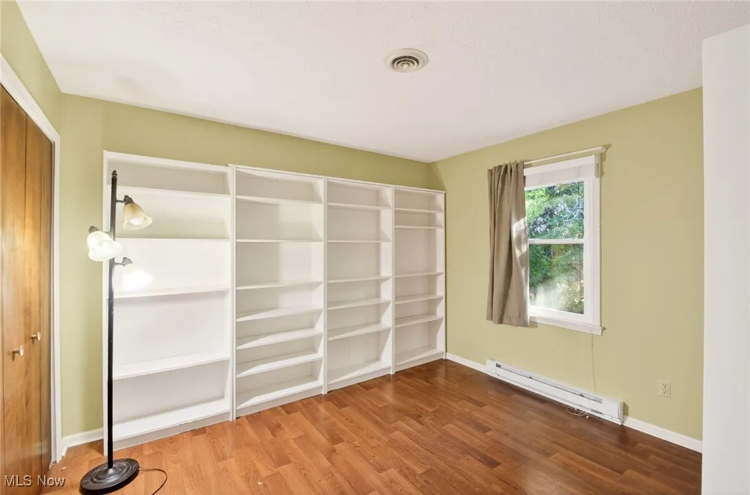 Unfurnished bedroom featuring a closet, baseboard heating, and dark wood-style floors