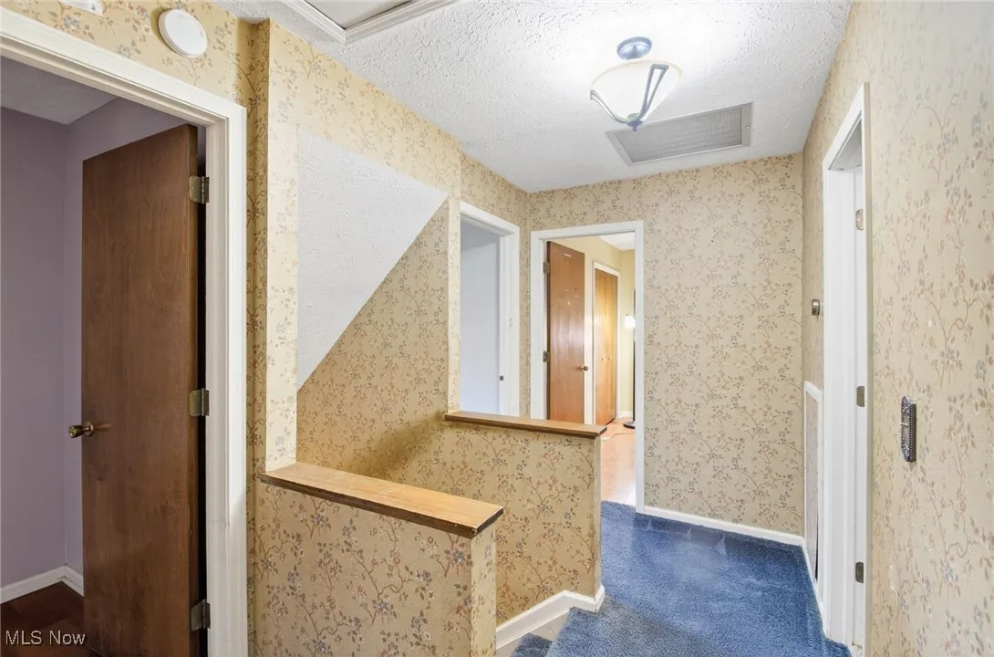 Hallway with wallpapered walls, a textured ceiling, and an upstairs landing