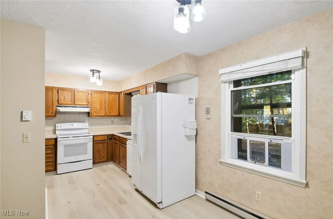 Kitchen with white appliances, light countertops, brown cabinetry, a textured ceiling, and light wood-style flooring