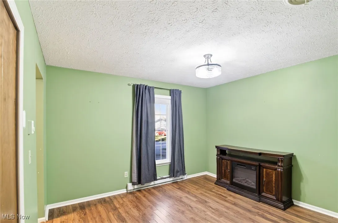 Unfurnished bedroom with wood finished floors, baseboard heating, and a textured ceiling