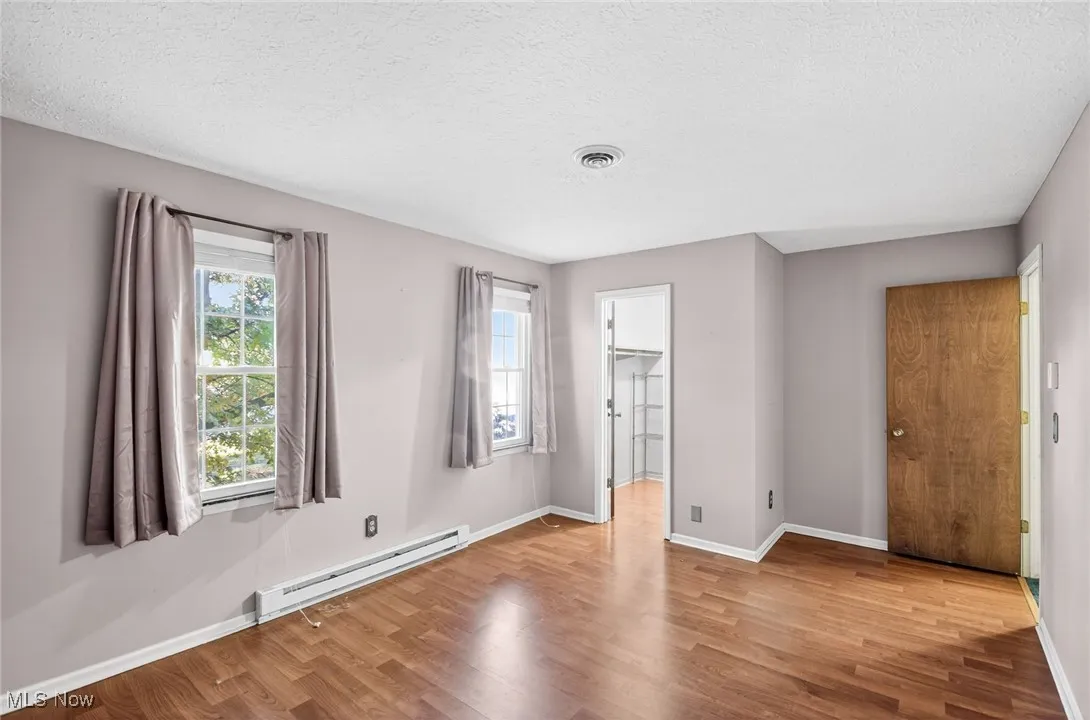 Unfurnished bedroom featuring a baseboard radiator, a spacious closet, a textured ceiling, and wood finished floors