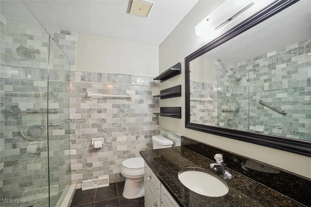 Bathroom featuring tile walls, vanity, dark tile patterned floors, wainscoting, and a stall shower