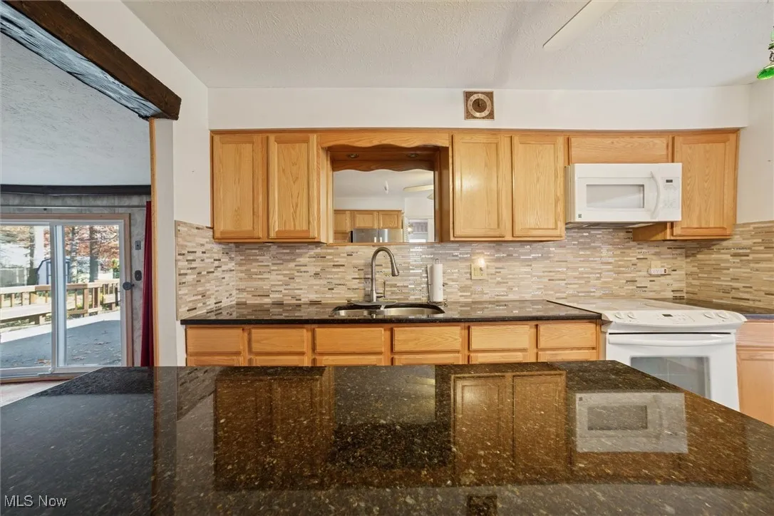 Kitchen featuring backsplash, dark stone counters, a textured ceiling, white appliances, and light brown cabinetry
