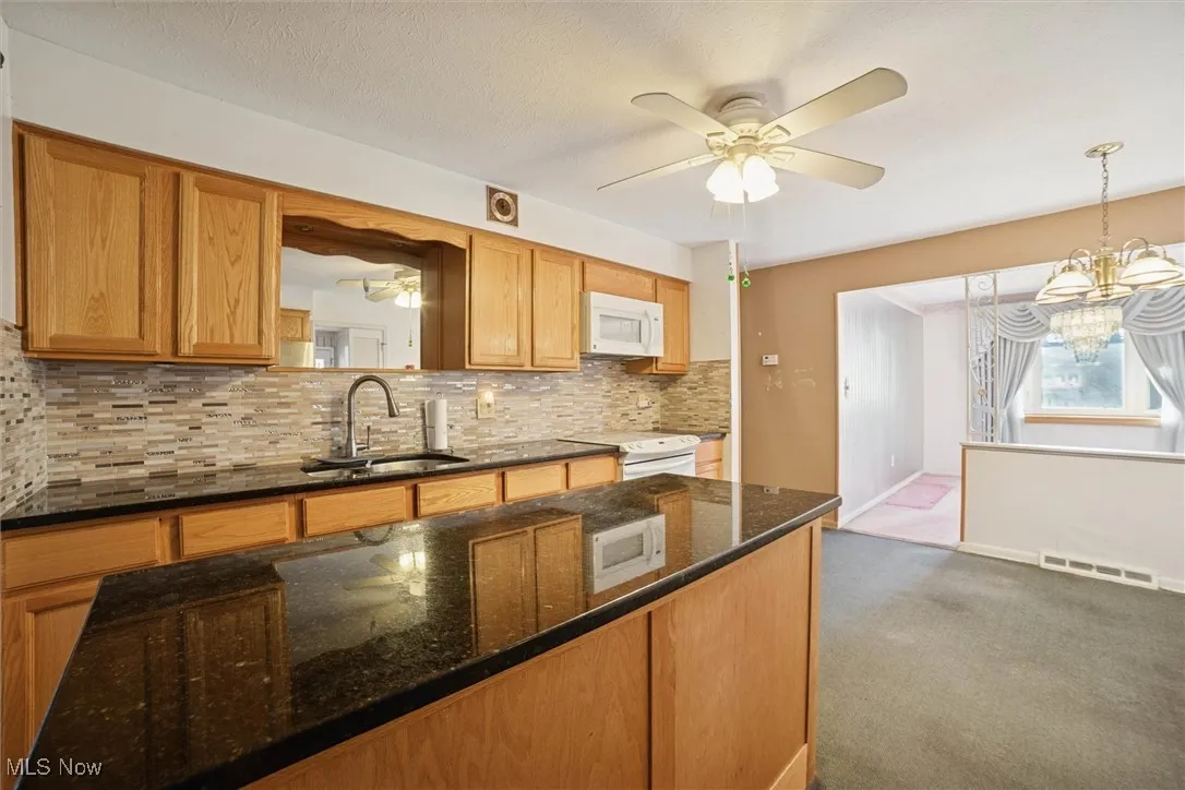 Kitchen with a ceiling fan, dark stone countertops, decorative backsplash, and dark carpet