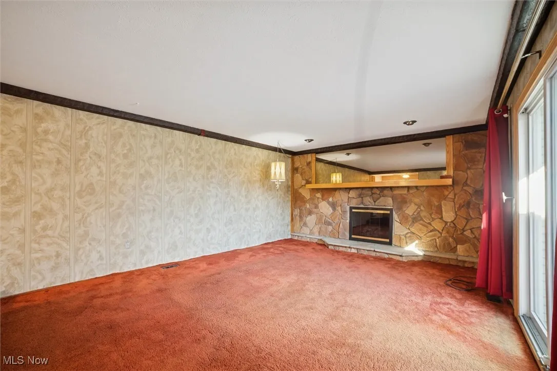 Unfurnished living room with ornamental molding, a stone fireplace, and carpet