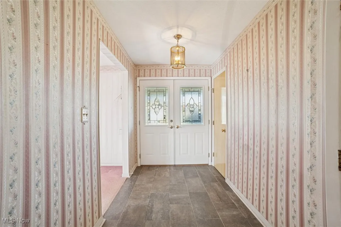 Doorway to outside with wallpapered walls, french doors, and a chandelier