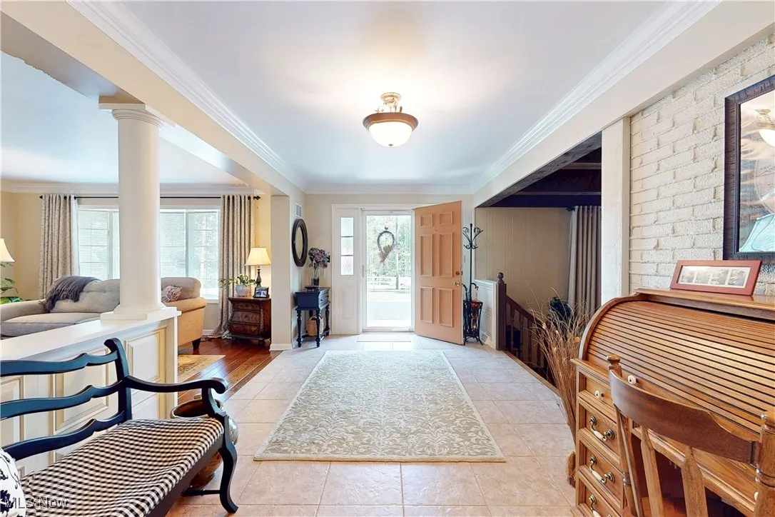 Foyer entrance with ornamental molding, plenty of natural light, light tile patterned floors, and decorative columns