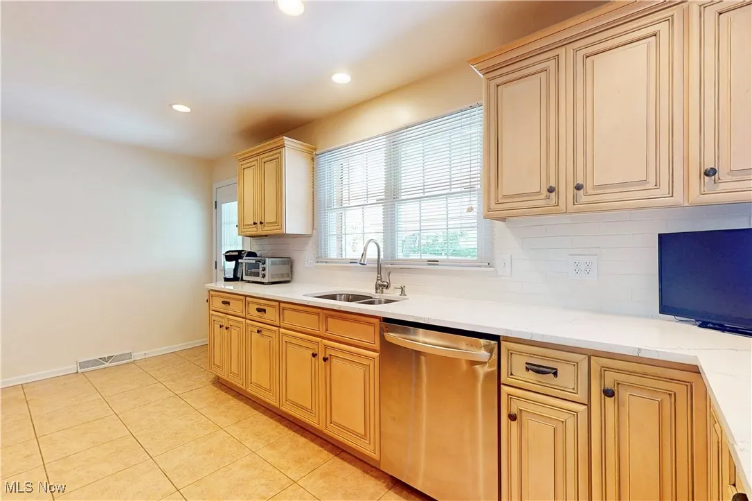Kitchen with stainless steel dishwasher, decorative backsplash, light tile patterned flooring, recessed lighting, and light stone countertops