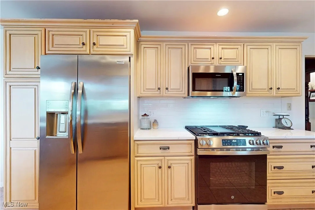 Kitchen with appliances with stainless steel finishes, cream cabinetry, backsplash, light stone countertops, and recessed lighting