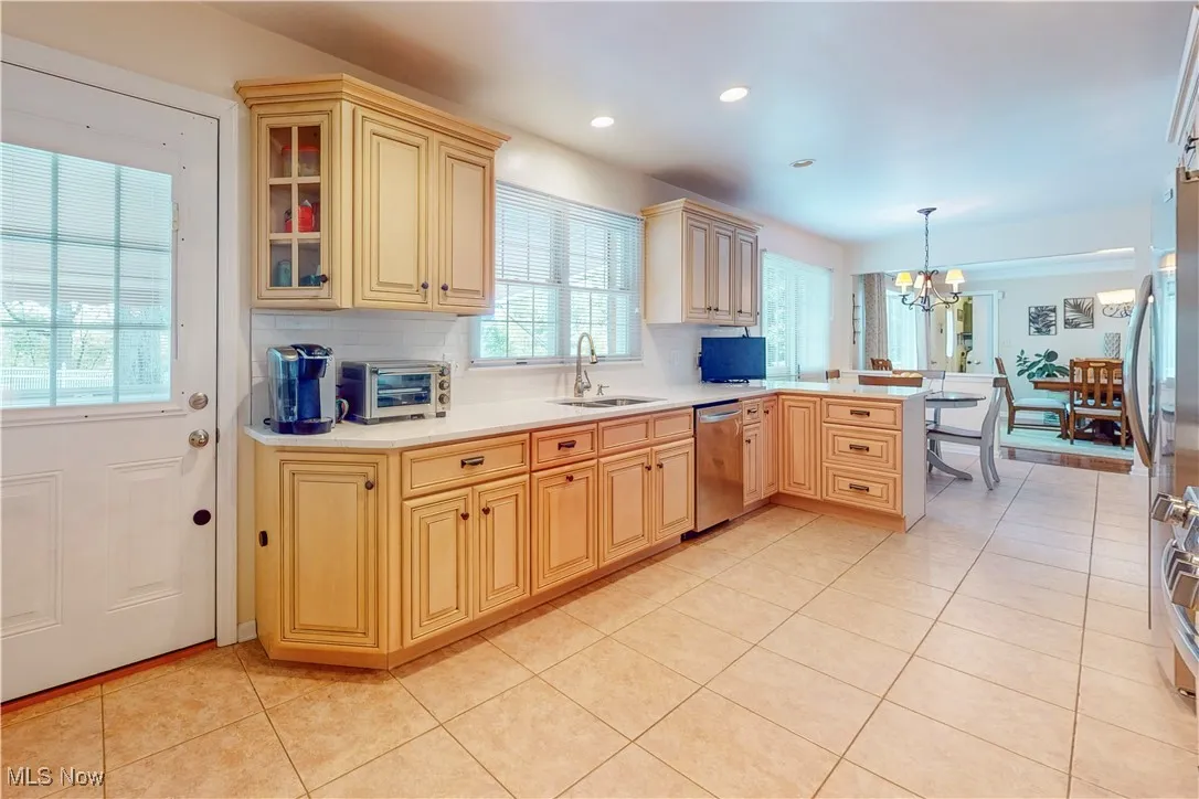 Kitchen with light tile patterned floors, hanging light fixtures, a chandelier, tasteful backsplash, and a peninsula