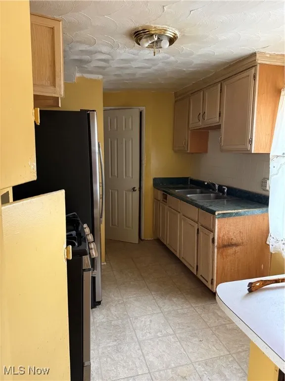 Kitchen featuring decorative backsplash, dark countertops, a textured ceiling, light brown cabinetry, and refrigerator