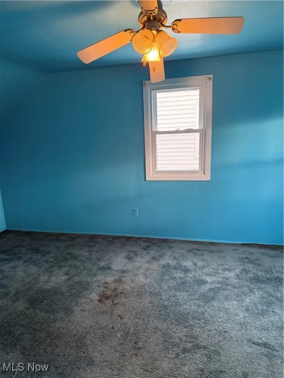 Spare room featuring dark colored carpet and a ceiling fan