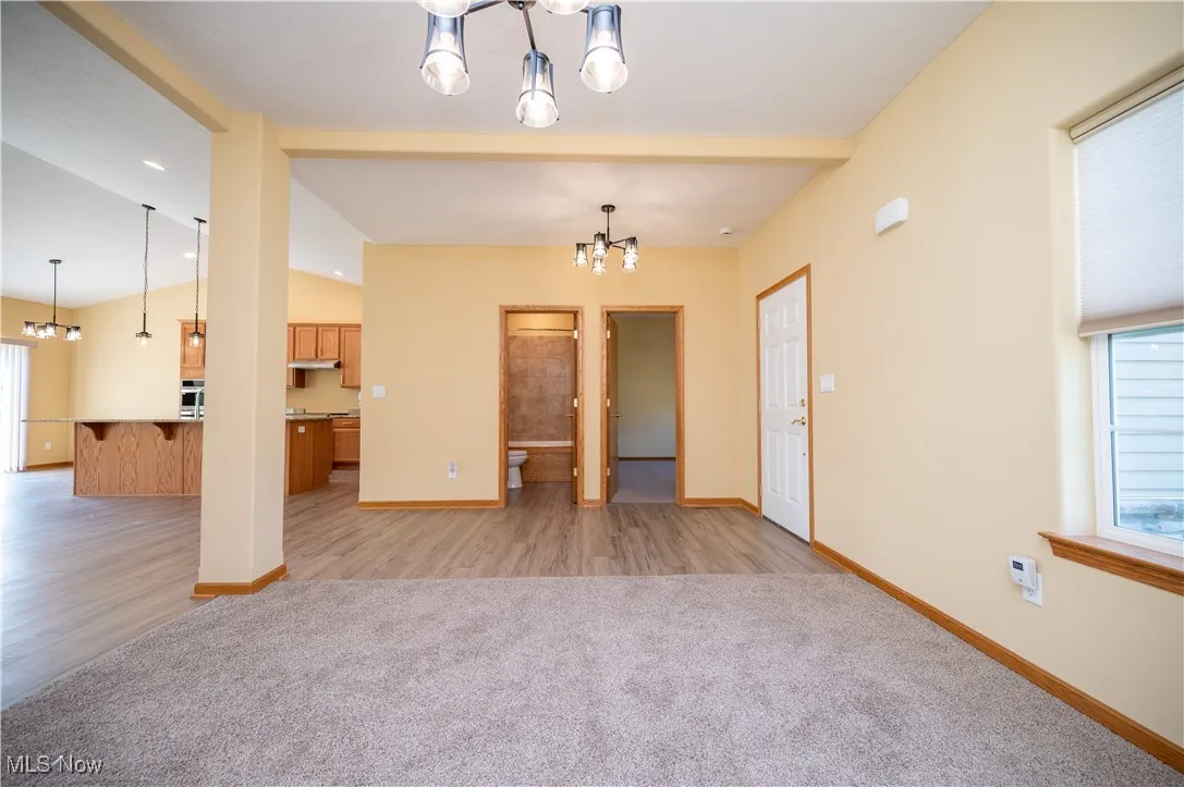 Unfurnished living room featuring a chandelier, light carpet, and light wood-type flooring