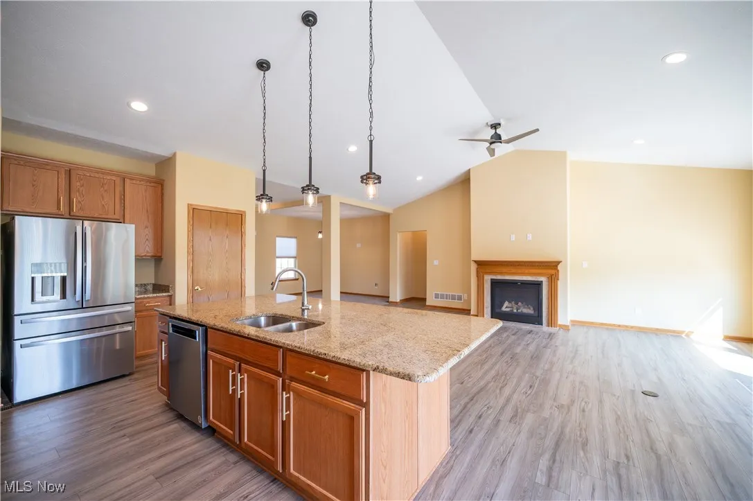 Kitchen featuring appliances with stainless steel finishes, pendant lighting, an island with sink, brown cabinets, and vaulted ceiling
