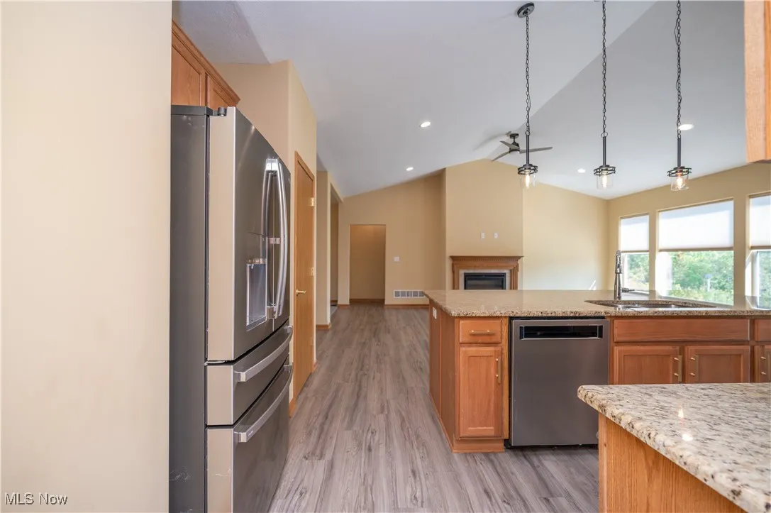 Kitchen featuring brown cabinetry, stainless steel appliances, hanging light fixtures, vaulted ceiling, and open floor plan