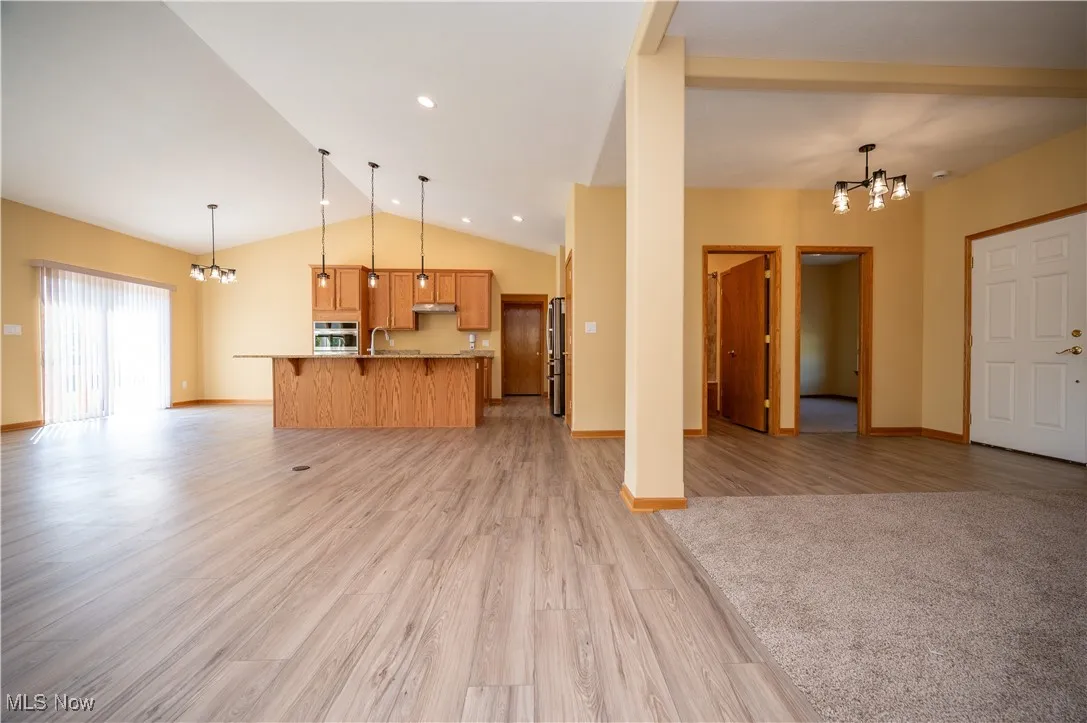 Unfurnished living room featuring a chandelier, light wood-style flooring, and vaulted ceiling