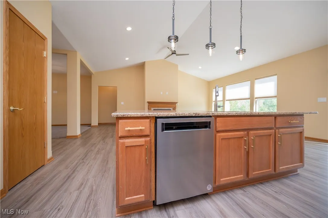 Kitchen with vaulted ceiling, light stone counters, dishwasher, decorative light fixtures, and open floor plan