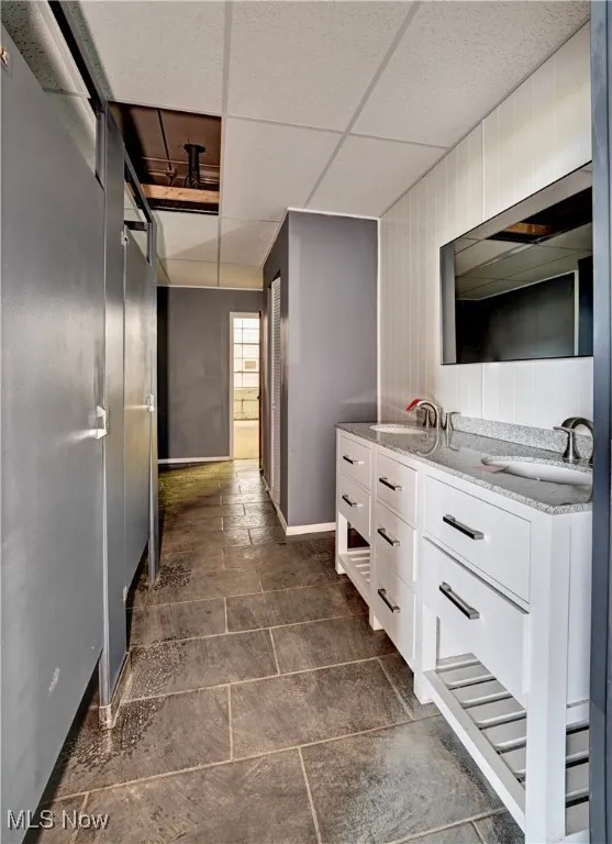 Bathroom with double vanity, a paneled ceiling, and stone tile floors