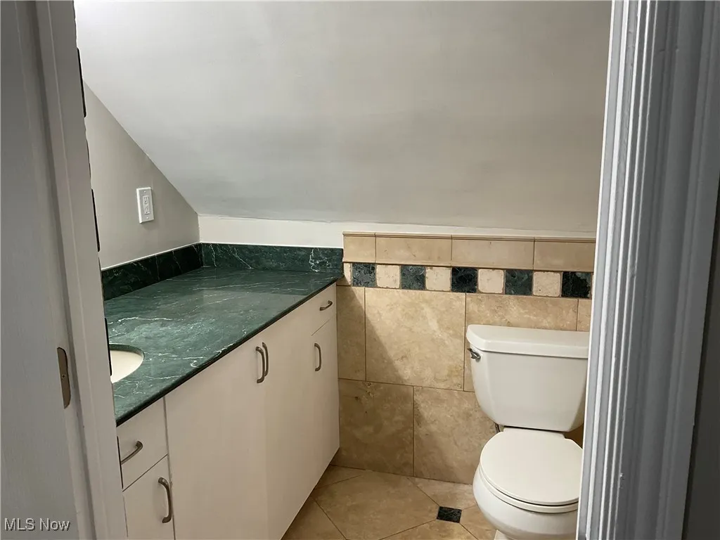 Bathroom featuring vanity, light tile off of Master Bedroompatterned flooring, tile walls, and lofted ceiling